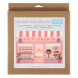 A counted cross stitch kit in its original brown kraft paper packaging, featuring a design of a pink and white bakery storefront with the word 'PATISSERIE' and a small blue 'trimits' brand label.