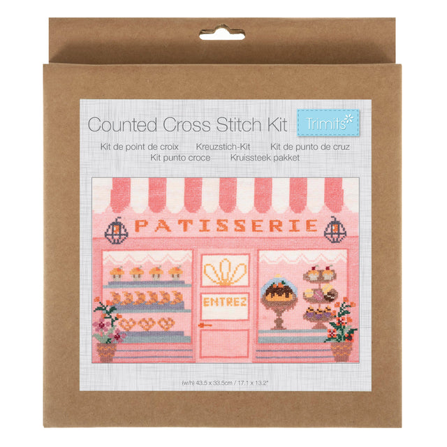 A counted cross stitch kit in its original brown kraft paper packaging, featuring a design of a pink and white bakery storefront with the word 'PATISSERIE' and a small blue 'trimits' brand label.