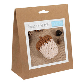 A brown kraft paper hanging bag package labeled 'Macramé Kit' with a small 'Trimits' logo, shown on a plain white background. The front has a photo window displaying a macrame acorn in brown and cream.