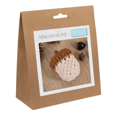 A brown kraft paper hanging bag package labeled 'Macramé Kit' with a small 'Trimits' logo, shown on a plain white background. The front has a photo window displaying a macrame acorn in brown and cream.