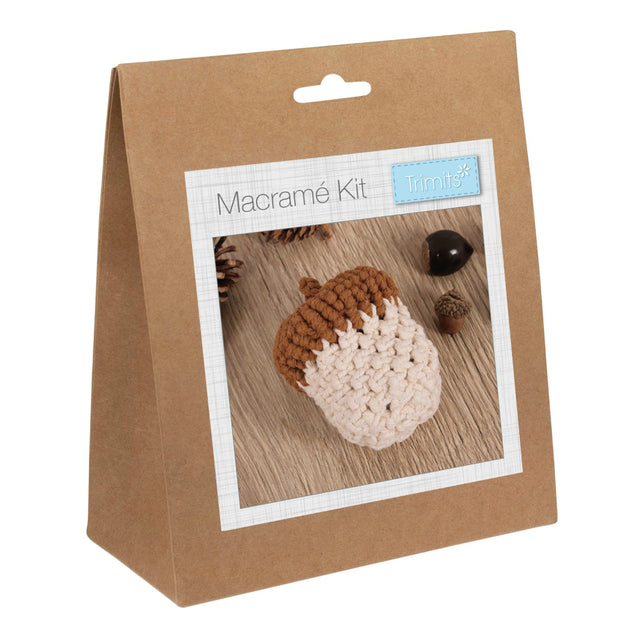 A brown kraft paper hanging bag package labeled 'Macramé Kit' with a small 'Trimits' logo, shown on a plain white background. The front has a photo window displaying a macrame acorn in brown and cream.