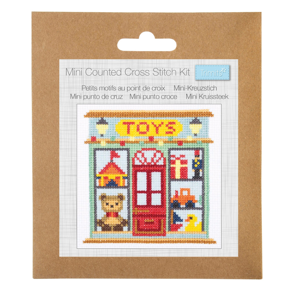 Mini Counted Cross Stitch Kit in its original brown kraft paper packaging, featuring a colorful cross-stitch design of a toy shop storefront.