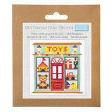 Mini Counted Cross Stitch Kit in its original brown kraft paper packaging, featuring a colorful cross-stitch design of a toy shop storefront.