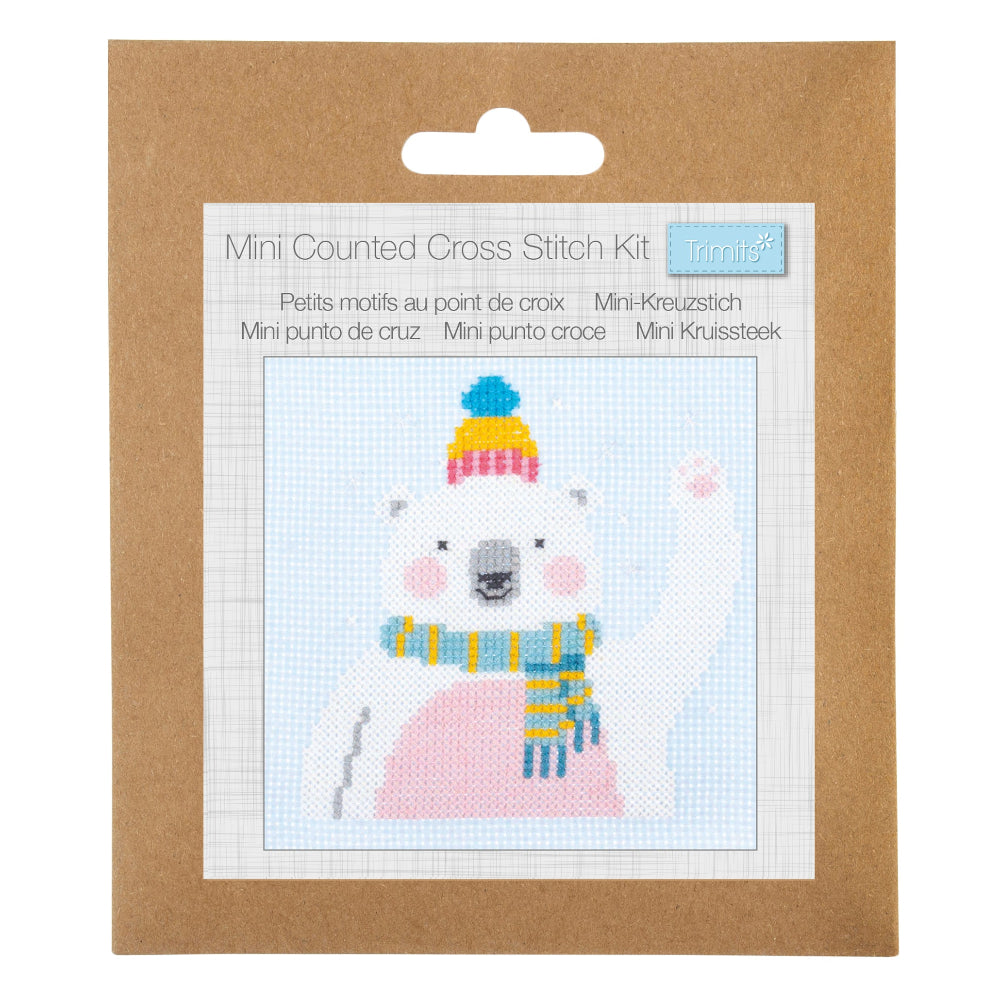 A mini counted cross stitch kit in its original brown kraft paper packaging, featuring a polar bear design with a pink body, blue and yellow striped scarf, and a colourful hat.