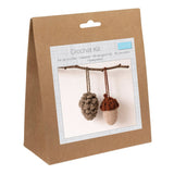 A brown kraft paper bag package for a crochet kit, featuring a front label with a photo of two crocheted acorns hanging from a twig.