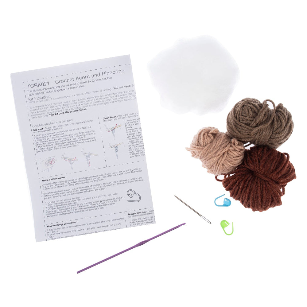 Crochet acorn and pinecone kit components on a white background, including a printed instruction sheet, white fiber ball, four yarn balls in beige, taupe, and brown, a metal hook, a blue stitch marker, a green stitch marker, and a purple crochet hook.