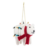 A white felt polar bear Christmas ornament with a red knit scarf, wrapped in multicolored holiday string lights, hanging from a gold string on a white background.