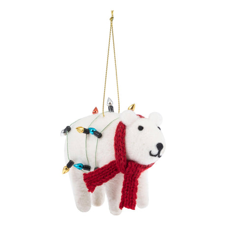 A white felt polar bear Christmas ornament with a red knit scarf, wrapped in multicolored holiday string lights, hanging from a gold string on a white background.