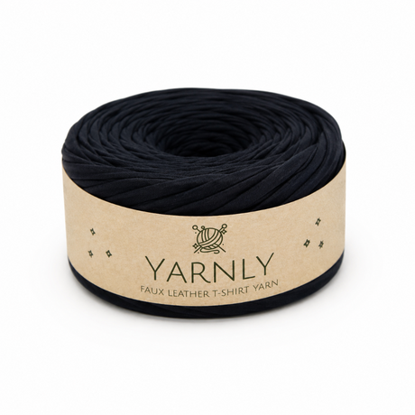 A roll of black faux leather t-shirt yarn wrapped in a beige paper band labeled 'YARNLY'.