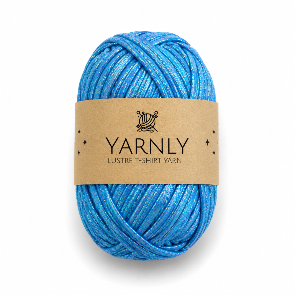 A ball of Yarnly Lustre T-shirt yarn with a brown paper label, featuring a shimmering blend of blue threads, on a white background.
