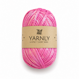 A skein of pink yarn with a shimmering glitter finish, wrapped in a brown paper band labeled 'YARNLY LUSTRE T-SHIRT YARN' on a white background.