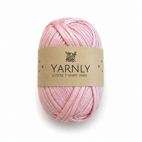 A skein of Yarnly Lustre T-Shirt Yarn in a soft pink color with subtle shimmer, wrapped in a brown paper label, on a white background.