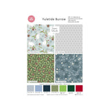 A fabric design card for 'Yuletide Burrow' by Sarah Wheeler, showing four pattern swatches: white rabbits in a snowy landscape, a gray geometric pattern, green pinecones on a forest background, and blue-gray snowflakes. A pink 'The Fabric Shop' logo is visible in the top left, and colour swatches are shown at the bottom.